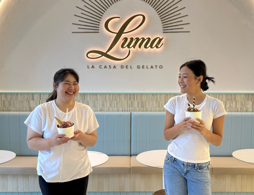 Two Luma team members laughing with gelato cups beneath the illuminated Luma sign